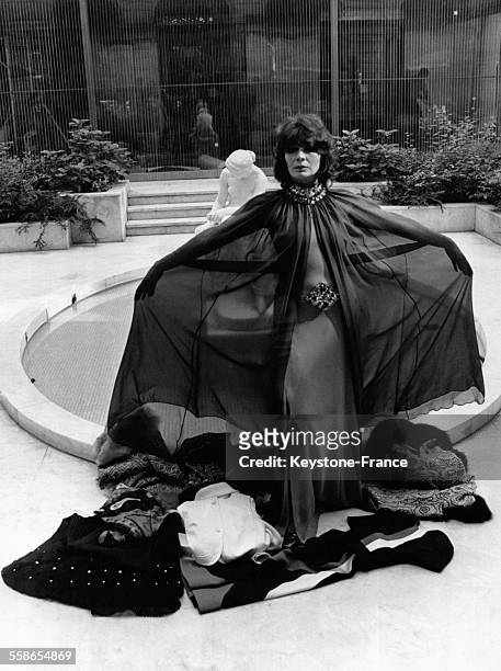 Juliette Greco presente une robe du soir et une cape en mousseline marron, a ses pieds d'autres modeles du Salon de la boutique, qui l'a choisie...