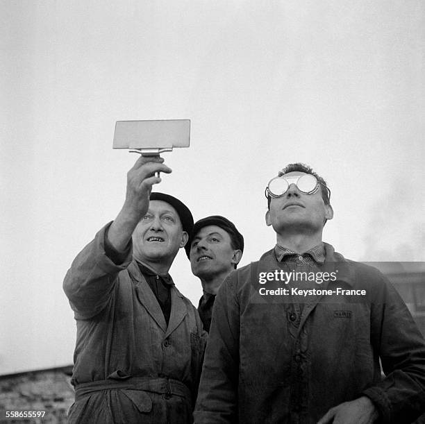 Trois hommes utilisant un verre fumé et des lunettes de soudeur pour regarder l'eclipse du soleil à Paris, France le 15 février 1961.