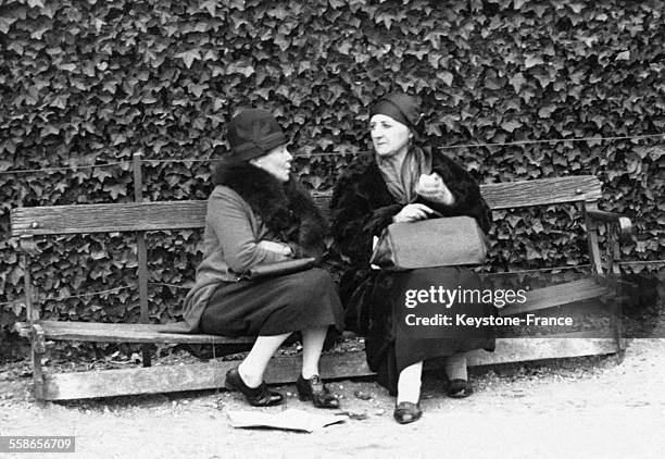 Deux femmes d'âge mûr discutent, assises sur un banc dans un jardin public à Paris, France.