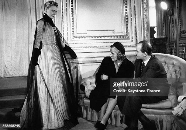 Le Prince Otto de Habsbourg et sa fiancee la princesse Regina de Saxe-Meiningen, chez le grand couturier Jean Desses, regardent un mannequin qui leur...