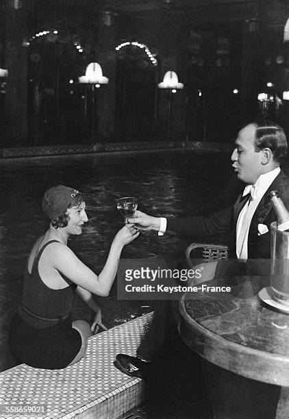 Femme en maillot de bain au bord de la piscine avec une coupe de champagne lors d'une nuit de fête au Lido, à Paris, France en 1930.