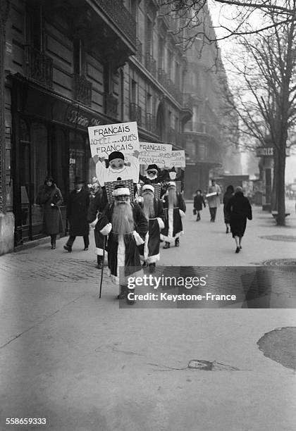 Trois hommes-sandwichs déguisés en Père Noël se promenant dans la rue et portant un écriteau où l'on recommande aux mamans françaises d'acheter des...