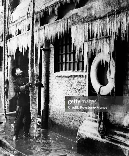 Homme dans un entrepôt de thé et de caoutchouc des docks de Londres qui vient d'être ravagé par un incendie et où on voit des stalactites formées par...