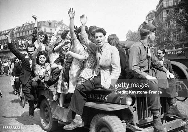 Des jeunes femmes et des jeunes hommes avec un GI sur une Jeep de l'armée américaine bras en l'air dans la rue à Paris, France, le 8 mai 1945.