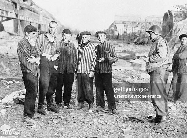 Cinq hommes en tenue de bagnards à rayures avec un militaire américain, au camp de Dora détruit par les combats, à Nordhausen-Dora, Allemagne, en...