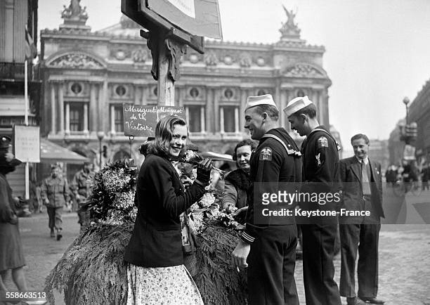 Deux marins offrent un bouquet de muguet à une jeune femme devant l'Opéra Garnier, à Paris, France, le 1er mai 1945.