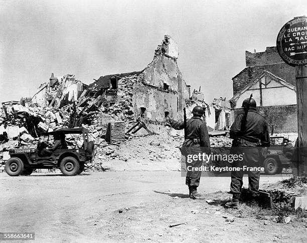 Deux militaires indiquent la route aux jeep, face à des maisons bombardées, à Saint-Nazaire, France, en mai 1945.