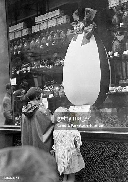 Deux fillettes regardant l'oeuf de Pâques géant dans la vitrine d'une confiserie à Paris, France le 3 avril 1931.