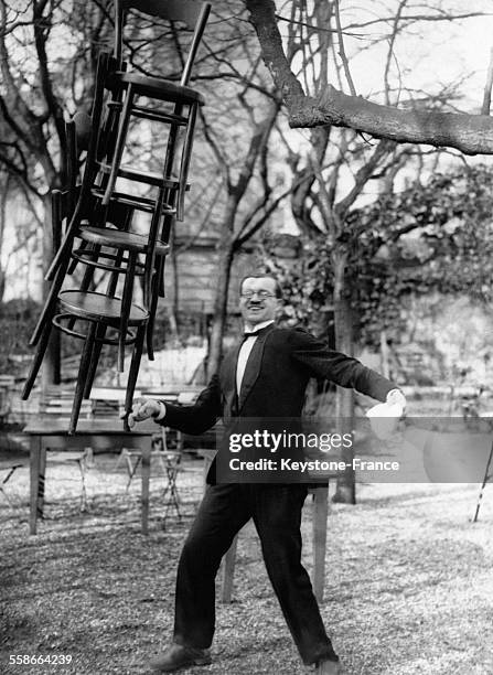 Monsieur Giraudi, maître d'hôtel équilibriste, maintenant quatre chaises en équilibre en tenant l'une d'elles par un pied entre deux doigts, en...