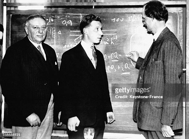 Le Professeur suisse Auguste Piccard, à droite, écrite une équation à la craie sur le tableau noir du MIT devant Karl Compton, président de...
