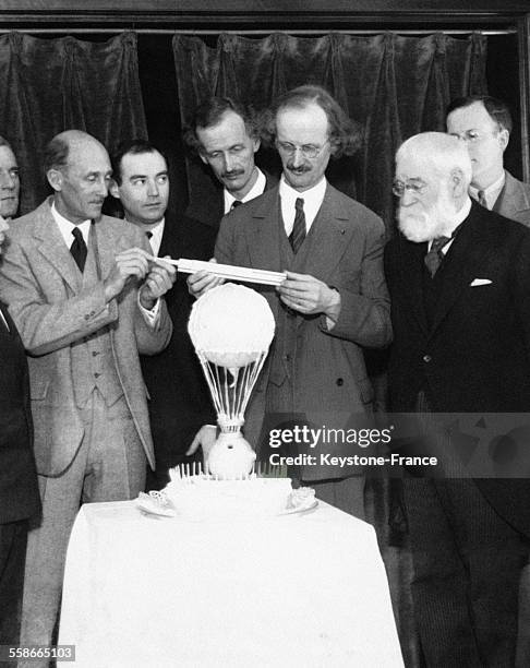 Le Professeur Auguste Piccard mesure son gâteau d'anniversaire en forme de ballon, en compagnie de sommités de l'aviation, de gauche à droite:...