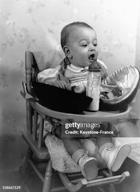 Un très jeune enfant dans sa chaise haute regarde un oeuf de Pâques ouvert en deux moitiés devant lui, à côté de son biberon.