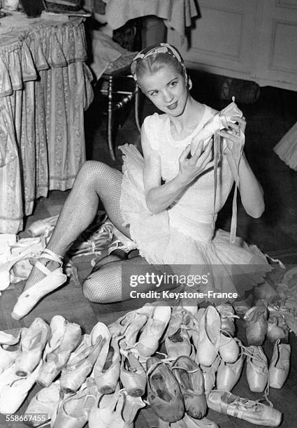 Une danseuse assise par terre au milieu d'un grand nombre de chaussons de danse usés.