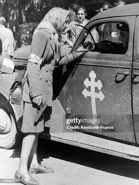 Une jeune FFI, armée d'un revolver, discute avec le conducteur d'une voiture avec la croix de Lorraine, à Paris, France en août 1944.