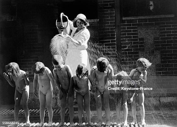 Une femme arrose à l'aide d'un arrosoir les enfants de l'école maternelle afin de les rafraîchir par la chaleur estivale, circa 1930 à Dugny, France.