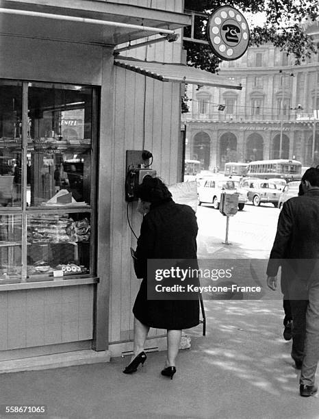 Une femme s'apprête à passer un coup de téléphone à une cabine téléphonique de rue protégée par un auvent le 17 avril 1962 à Rome, Italie.