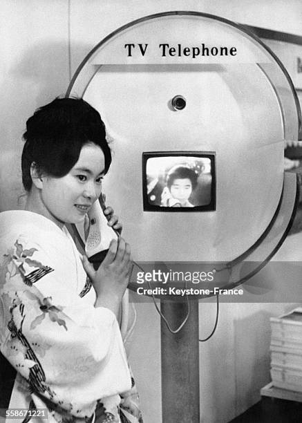 Une femme japonaise en kimono fait la démonstration depuis un bateau japonais du TV-Téléphone en tenant le combiné téléphonique en main tandis que...