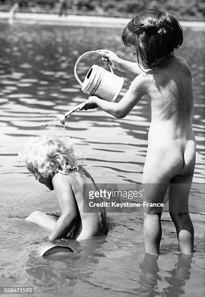 Une petite fille munie d'un arrosoir verse de l'eau sur les cheveux d'un jeune enfant assis dans l'eau le 11 juin 1937 en Allemagne.