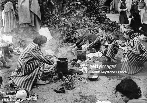 Femmes juives préparant leur repas, derrière une pile de chaussures ayant appartenu à des internés morts dans le camp de Bergen-Belsen, circa 1940,...