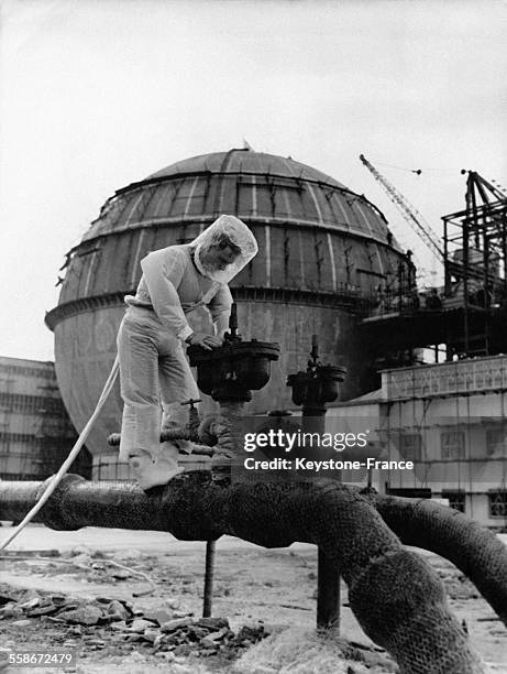 Un technicien vêtu d'une combinaison de protection examine l'étanchéité des vannes dans un centre de recherche atomique le 10 mai 1957 à Dounreay,...