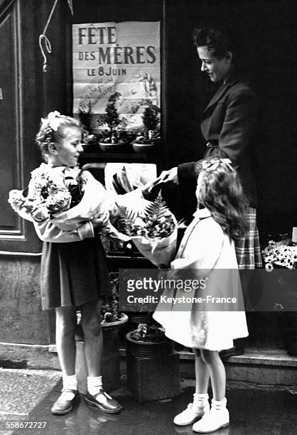 Deux petites filles sortent les bras chargés de fleurs d'une boutique de fleuriste où elles ont acheté un bouquet pour leur mère à l'occasion de la...