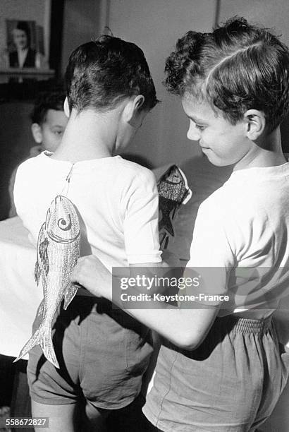 Un petit garçon accroche un poisson d'avril dans le dos de son frère pendant que ce dernier en prépare un le 29 mars 1963 en France.