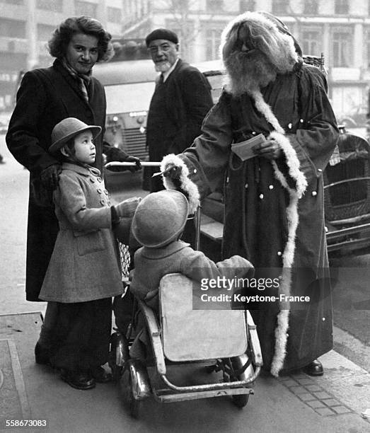 Deux petites filles en poussette ont rencontré le Père Noël sur le trottoir devant les grands magasins, circa 1940 à Paris, France.