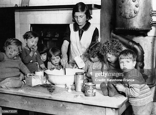 Une femme prépare le Christmas pudding sous l'oeil attentif de très jeunes enfants rassemblés autour de la table.