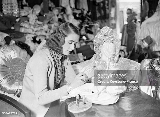 Une femme met du rouge sur les lèvres de la poupée, comme la nouvelle mode le veut, à Paris, France le 30 décembre 1931.