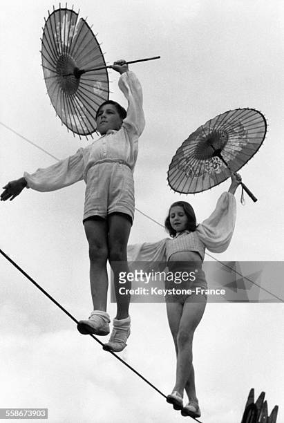 Sonja et Alex, deux enfants funambules dans un cirque, marchent en équilibre sur un fil en portant une ombrelle.