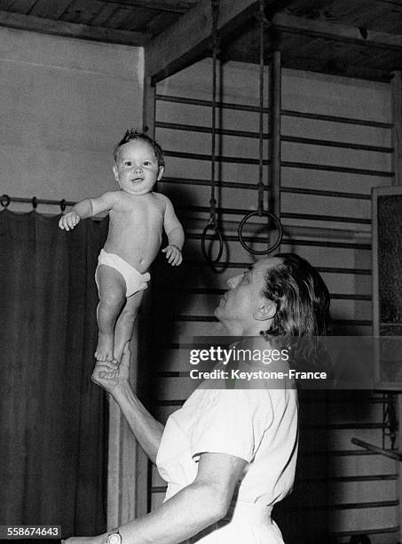 Un très jeune enfant tient en équilibre sur la pointe d'un pied posé sur la main de son père.