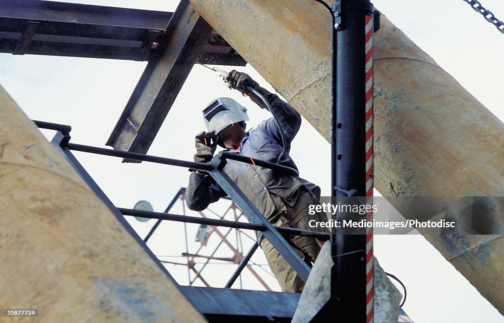 Welder repairing beam on construction site, low angle view