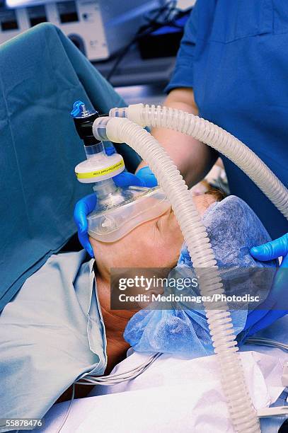 female nurse holding an oxygen mask on a patient's face - man lying on operating table stock pictures, royalty-free photos & images