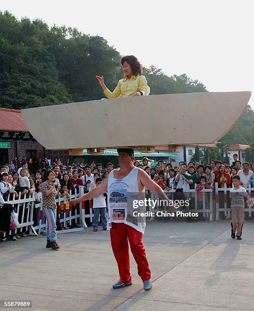 John Evans, a strongman from Britain, carries a boat and a woman on his head during his performance to mark the Chinese National Day at East Lake...