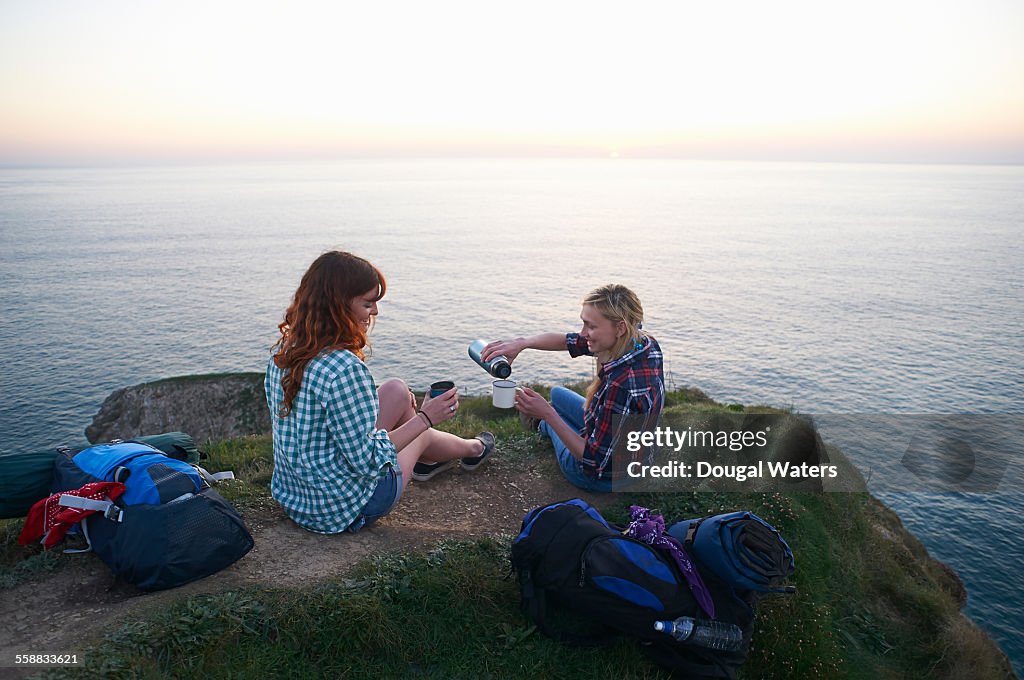 Hikers pour hot drink on cliff top