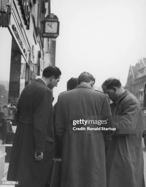 Group of street traders, involved in the illegal sale of nylon stockings, chat to a contact man on Oxford Street, London, 10th February 1951....