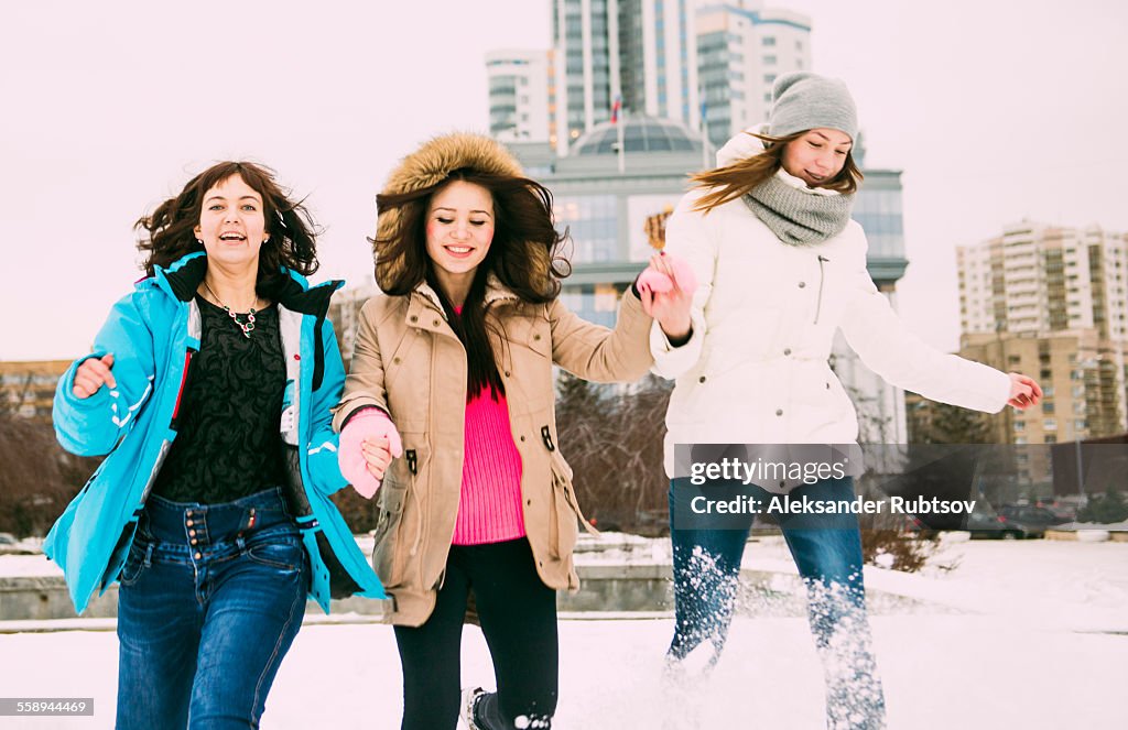 Three young women running in snow holding hands