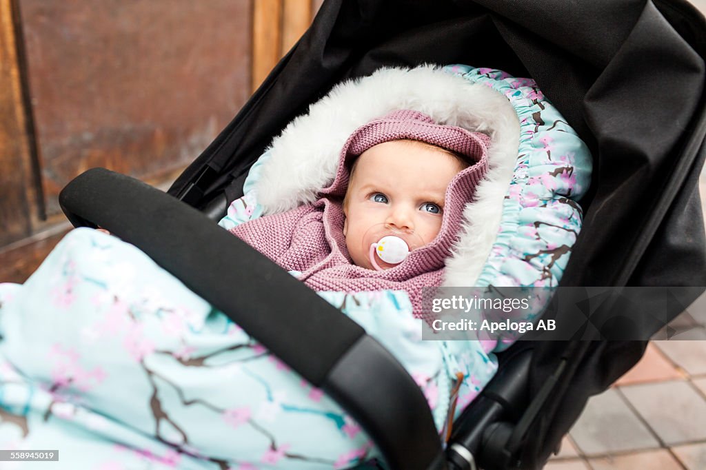 Cute baby girl with pacifier in carriage looking away outdoors