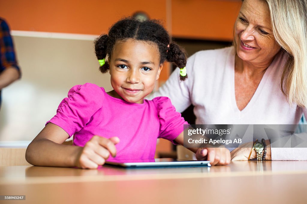 Happy teacher with girl using tablet computer at desk