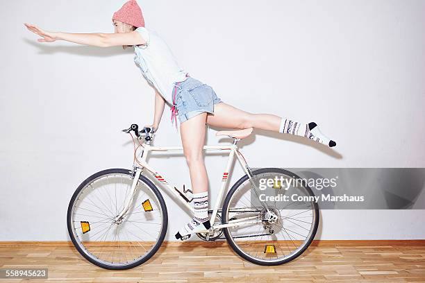 studio shot of young woman balancing on one leg on bicycle - velo humour stock-fotos und bilder