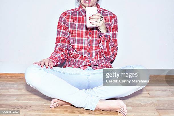 studio shot of young woman sitting on floor drinking juice - ジュースパック ストックフォトと画像