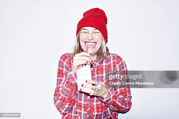 studio portrait of young woman in red hat drinking juice - ジュースパック ストックフォトと画像