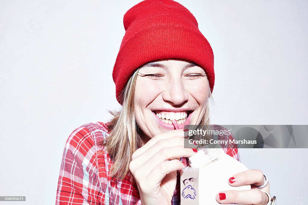 Close up studio portrait of young woman in red hat drinking juice