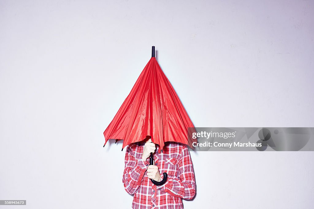 Studio shot of young woman holding red umbrella over her head
