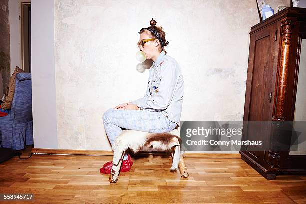 young woman sitting on hassock wearing sunglasses and blowing bubblegum - bizzarro foto e immagini stock