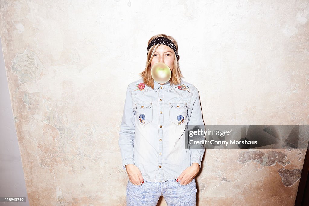 Studio shot of young woman blowing yellow bubble gum bubble
