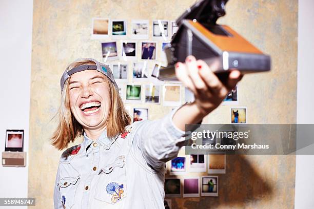 young woman in front of photo wall taking instant selfie on retro camera - blonde woman selfie foto e immagini stock