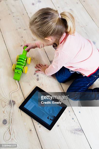 girl with digital tablet, playing toy on wooden floor - small child sitting on floor stock-fotos und bilder