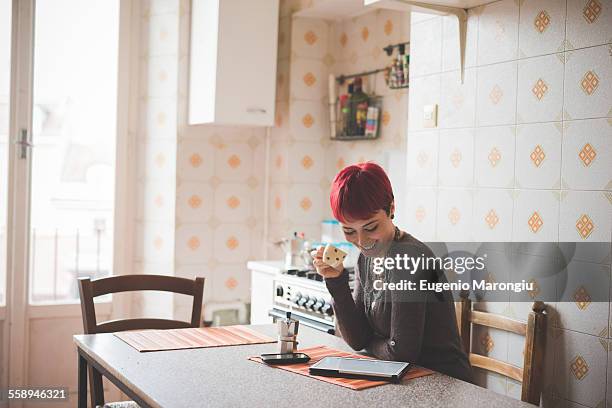 young woman sitting at table drinking coffee, looking at digital tablet - funky stockfoto's en -beelden