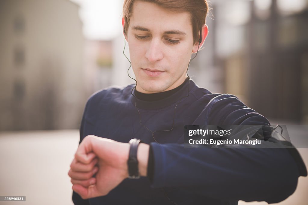 Young male runner checking wristwatch in city square